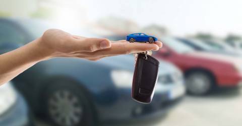 Hand met autosleutel en speelgoedauto met op de achtergrond auto's