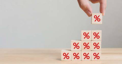 Hand die een houten kubusblok met percentage teken zet in opwaartse richting op dezelfde andere blokjes