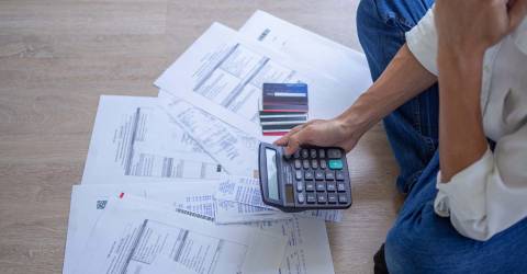Man met stress zit op de grond met allemaal rekeningen, creditcards en een rekenmachine